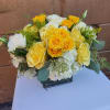 Low arrangement of yellow and white roses with white hydrangeas in a clear glass cube vase