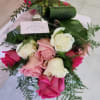 Hand-tied bouquet of pink and white roses with decorative greenery in clear wrap and a pink ribbon