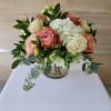Short round bouquet of peach and cream roses with white hydrangeas in a clear glass vase