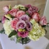 Low bouquet of pink roses, lavender lisianthus, and white hydrangeas in a clear glass vase