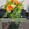Tall vase of yellow and orange roses with white blooms and trailing ivy
