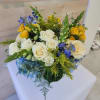Round arrangement of cream roses, yellow blooms and blue flowers in a compact mixed bouquet
