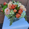 Low arrangement of peach roses and orange tulips with green hydrangeas in a clear glass vase
