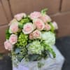 Round arrangement of pale pink roses with white and green hydrangeas in a clear glass vase