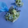 Blue and white wrist corsages with roses and hydrangea, accented with ribbon and pearls on a light background