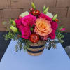 Compact arrangement of hot pink and peach roses in a striped woven basket container