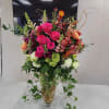 Tall arrangement of hot pink roses and mixed flowers in a clear glass vase with trailing ivy.