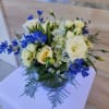 Low round arrangement of white and cream flowers with blue accents in a clear glass vase