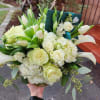 Low arrangement of white roses, hydrangeas, tulips, and calla lilies in a clear glass vase with a green card.
