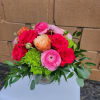 Short glass vase of pink roses, ranunculus, and green hydrangeas.