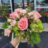 Small bouquet of pink roses with green hydrangea in a clear glass vase held outdoors.