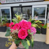 Compact arrangement of bright pink roses and mixed blooms in a small decorative vase, held outside a flower shop.