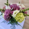Low arrangement of lavender roses, white blooms, green hydrangea and trailing fern in a compact bouquet.