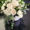 White and cream rose arrangement with greenery in a white textured pot on a black table