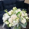 Low round arrangement of white and cream flowers in a silver container on a black table by a dark sofa