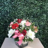 Bouquet of red, pink, and white flowers in a glass vase with a pink ribbon