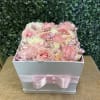 Pink and white roses arranged in a white box with a pink ribbon