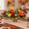 Autumn floral centerpiece in a gold bowl with red, yellow, and orange blooms