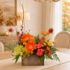 Orange and red floral arrangement in a wooden box on a dining table