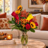 Autumn bouquet of roses, sunflowers, lilies, and mums in a glass vase
