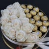 White roses and gold-wrapped chocolates in a round gift box with a ribbon