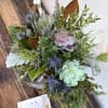 Succulent arrangement with blue thistle-like blooms in a glass vase