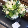 White rose and green floral arrangement in a glass vase on a piano bench