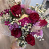 Handheld bouquet of red roses and pink-purple flowers in a clear vase
