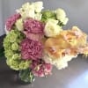 Bouquet of pink carnations, white roses, green hydrangeas, and orange orchids in a glass vase