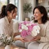 Pink and white flower arrangement in a round box held by two women