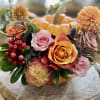 Autumn floral arrangement with roses and dahlias around a small pumpkin