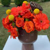 Orange roses and gerbera daisies in a brown face vase