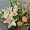 Cream roses and white lilies arranged in a dark vase