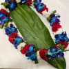 Floral lei with blue orchids, red carnations, and white flowers on a large green leaf