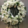 White floral wreath on a black easel with a ribbon bow