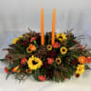 Low floral centerpiece with two orange taper candles and mixed autumn blooms