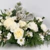 White floral arrangement with roses and daisies around an angel figurine