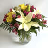 Bouquet of white lilies, pink flowers, and yellow chrysanthemums in a glass vase
