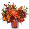 Orange roses and mixed fall flowers in a striped glass vase