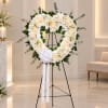 White floral heart wreath on a black stand with a white ribbon bow