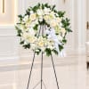 White floral wreath on a black stand with a white ribbon