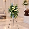 Standing funeral spray with white lilies, roses, and blue flowers on an easel