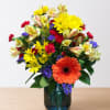 Mixed bouquet in a blue glass vase with orange, yellow, red, and purple flowers