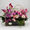 Pink and purple floral arrangement in a wooden box with roses and calla lilies