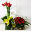 Red tulips and roses arranged in a glass vase with yellow orchids