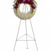 Standing round wreath of white flowers with red roses and blue blooms on a metal easel