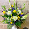 Tall yellow, white, and purple flower arrangement in a white pedestal vase