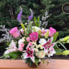 Pink roses and white lilies with accent blooms arranged in a low glass vase
