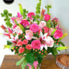 Tall mixed bouquet of pink roses and white-pink lilies in a clear glass vase with a pink ribbon.