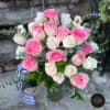 Arrangement of pink and white roses in a clear glass vase with striped ribbon